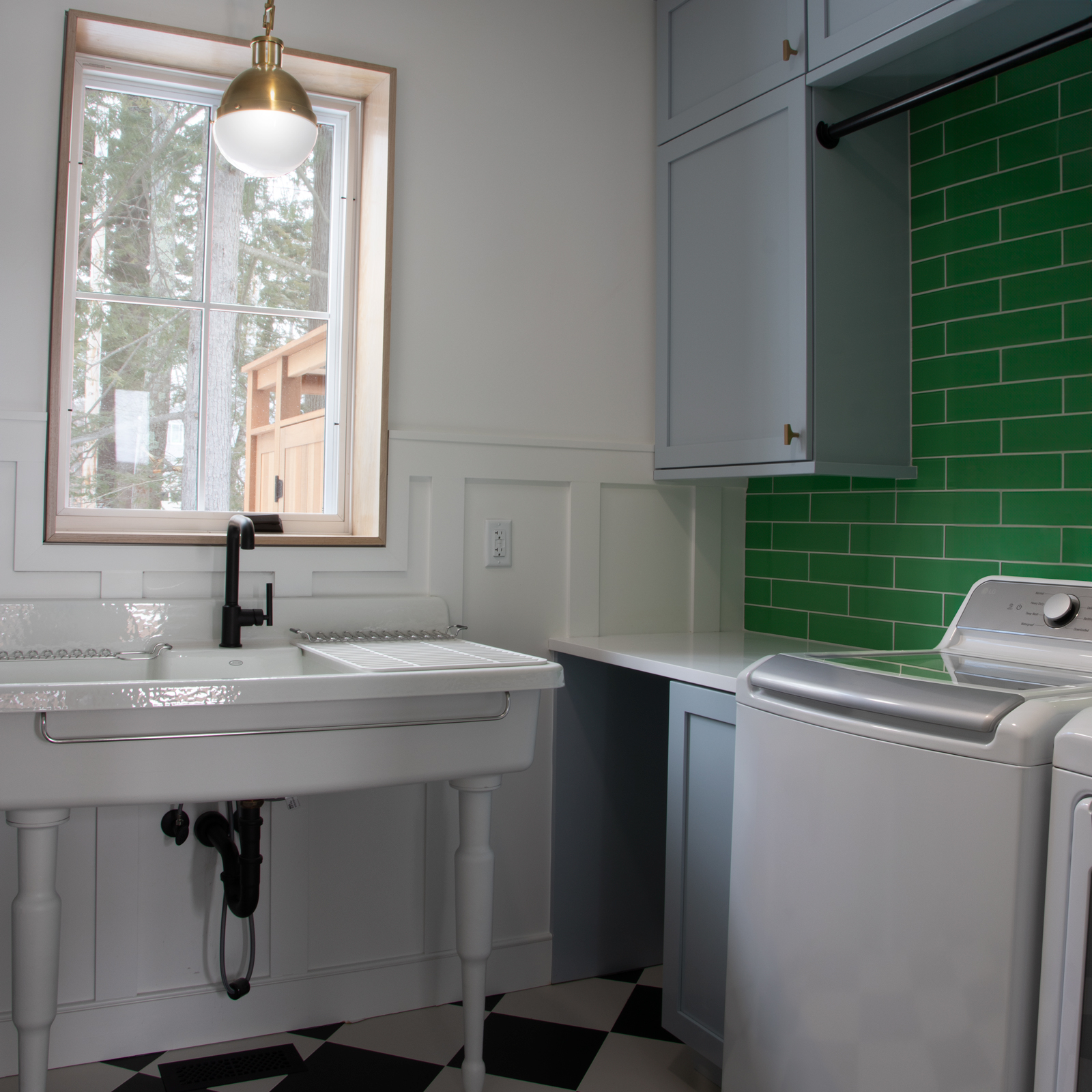 The Laundry Room is a fun take on a vintage farmhouse-style laundry room. Black and white checkered floor, vintage sink and Kelly green tile backsplash make this room pop. Peaking through the window you can spot the outdoor shower.