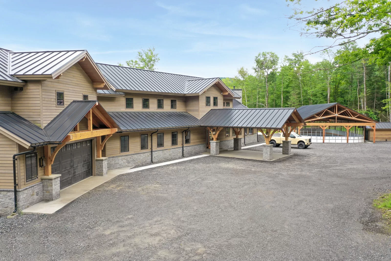 Large parking lot with ample space leads to a lodge entrance framed by stunning timber beams. The custom hockey rink features matching timber framing, blending rustic design with winter sports.